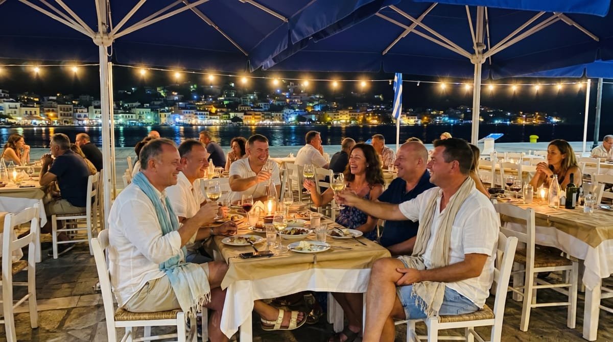 A group toasting wine at night beside the Poros harbor at Sti Rota.