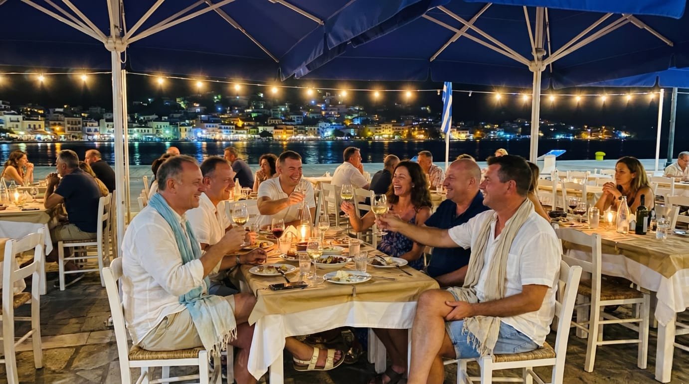A group toasting wine at night beside the Poros harbor at Sti Rota.